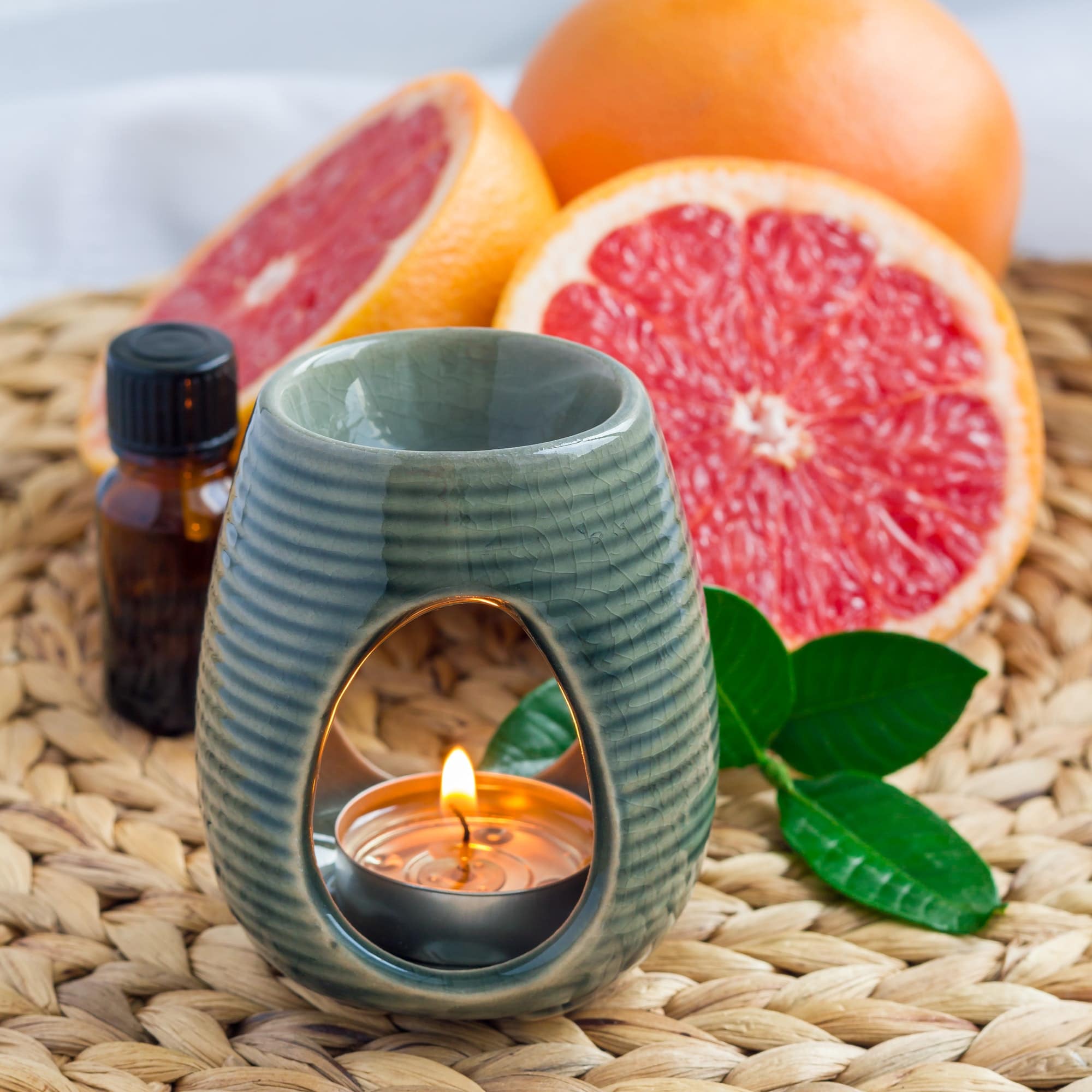Aroma lamp with grapefruit essential oil on woven mat, grapefruits on background, square format