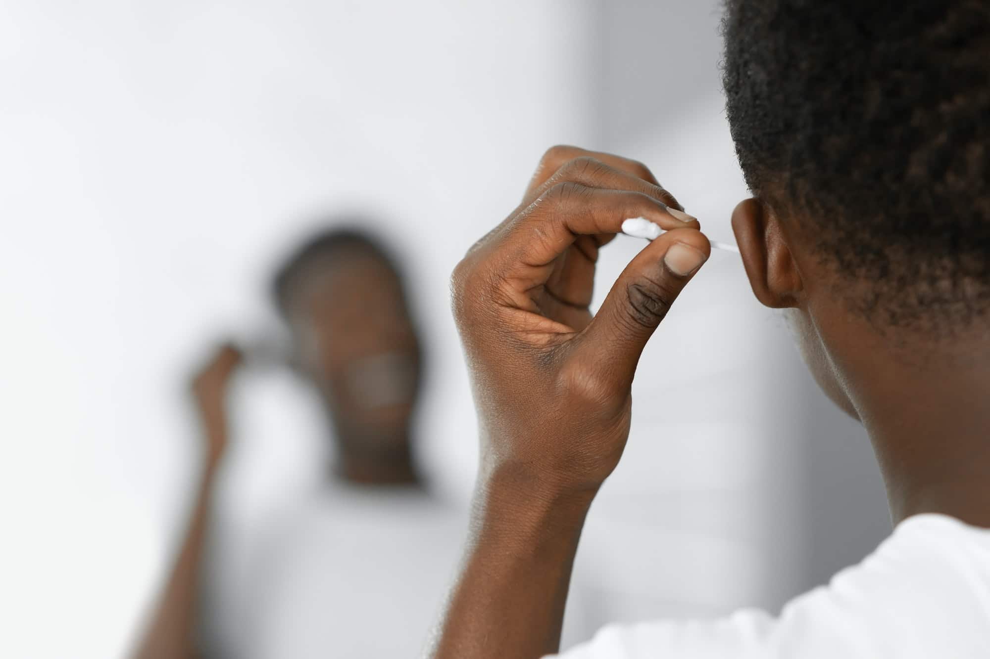 Black Man Cleaning Ears Using Cotton Swab Standing In Bathroom