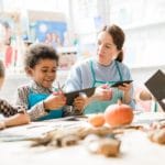Multiracial schoolkids and teacher in aprons cutting out halloween decorations