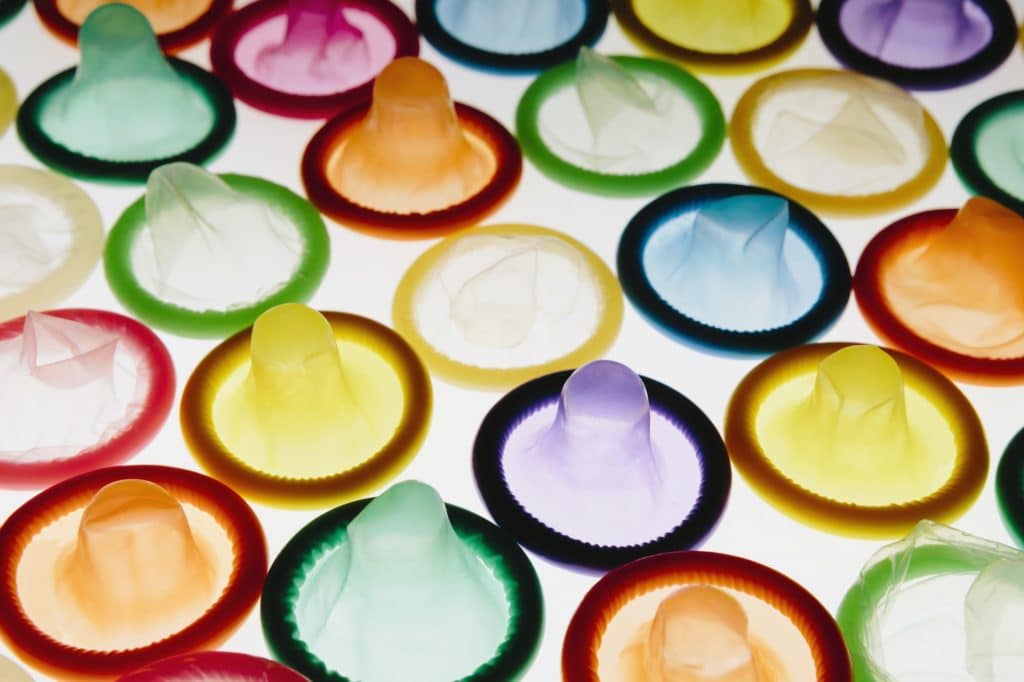 A large group of multi-colored condoms displayed on a white background. Laid out neatly.